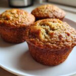 Close-up of three golden-brown banana protein muffins resting on a white plate.