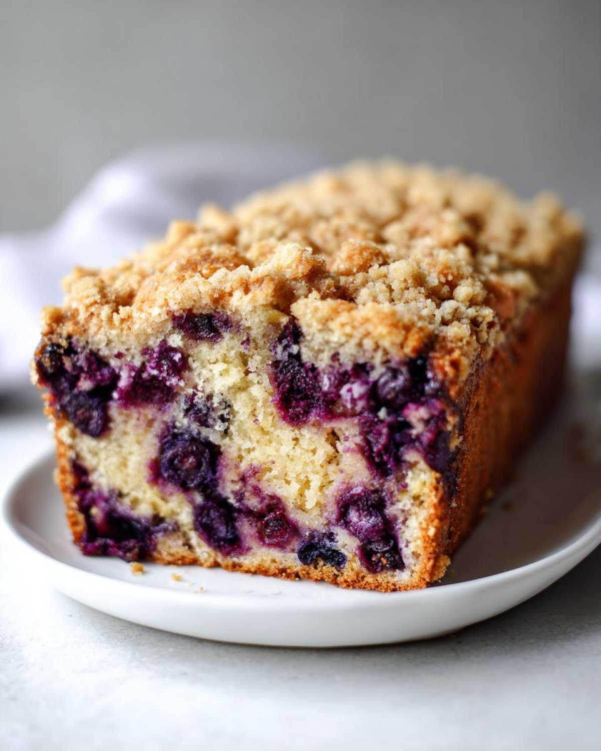 A close-up of a slice of blueberry banana bread featuring a moist crumb and a generous streusel topping.