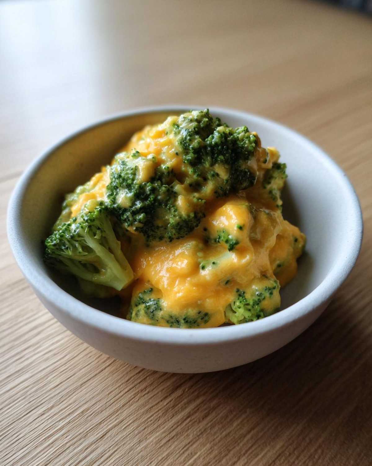 Close-up of steamed broccoli florets generously coated in a thick, creamy orange cheddar sauce, representing broccoli cheddar.