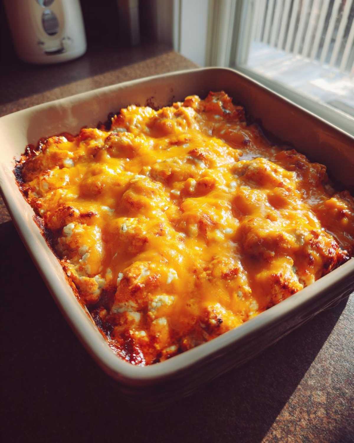 Hot, bubbly Buffalo chicken dip topped with melted orange cheddar cheese in a square baking dish.