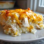 A square serving of cheesy chicken and rice bake topped with melted, slightly browned cheddar cheese.