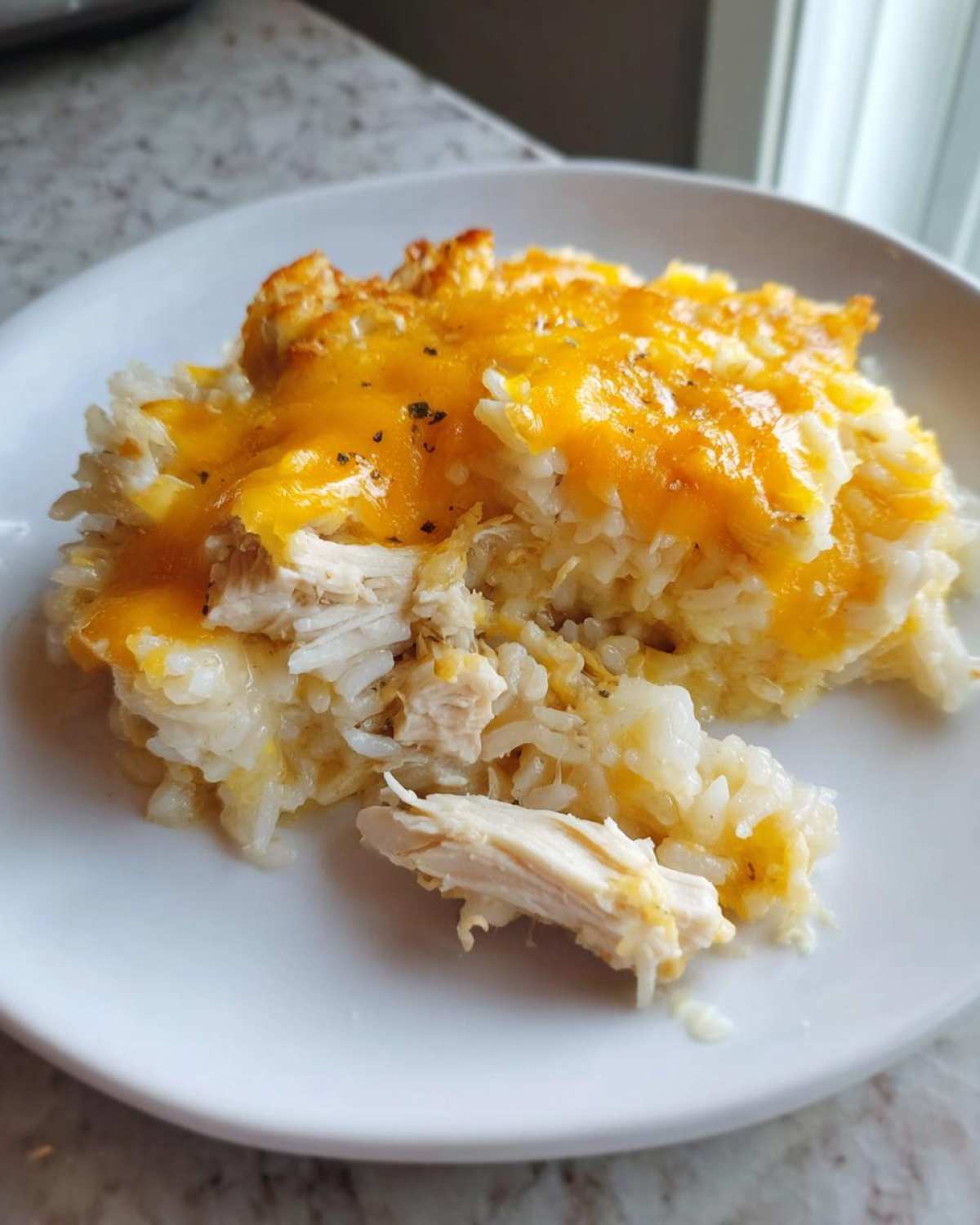 A close-up serving of cheesy chicken and rice bake topped with melted cheddar cheese on a white plate.