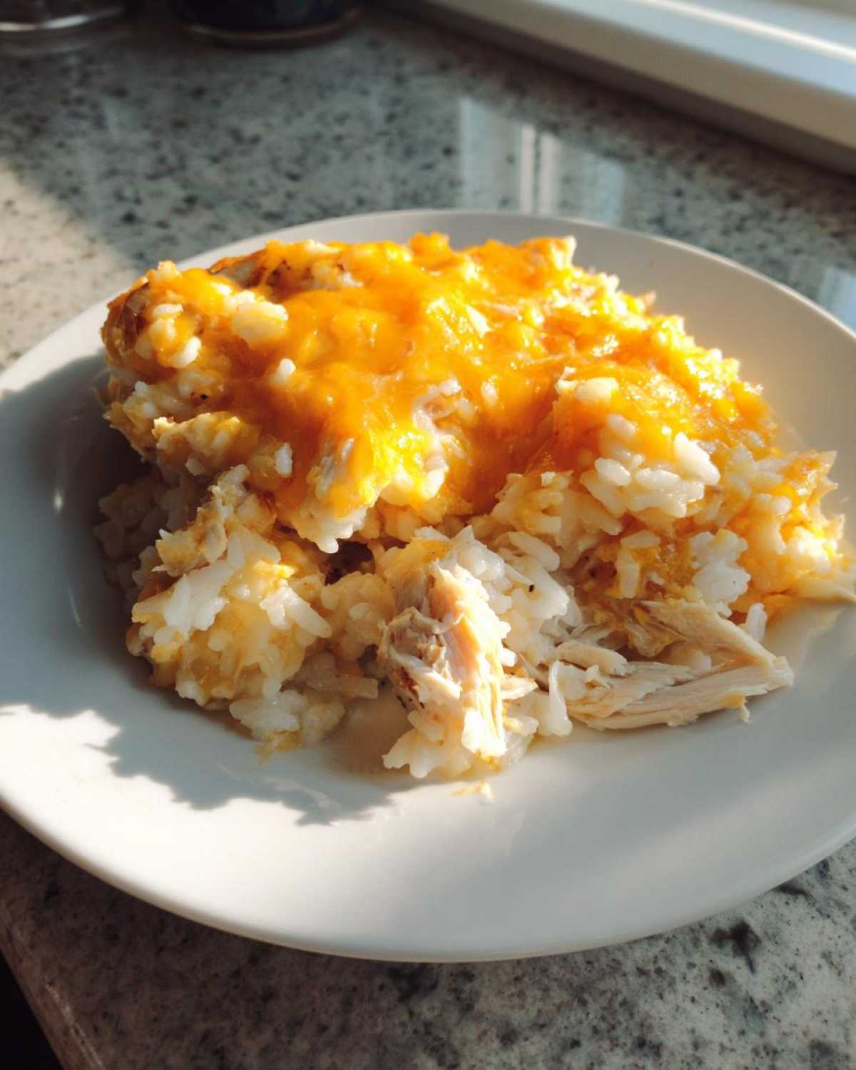 A serving of cheesy chicken and rice bake topped with melted orange cheddar cheese on a white plate.