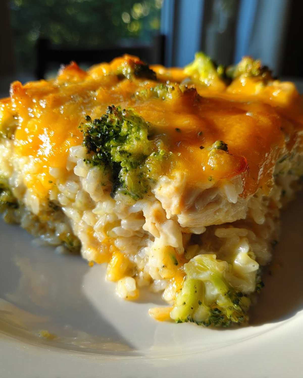 Close-up of a serving of creamy chicken broccoli rice casserole topped with melted cheddar cheese.