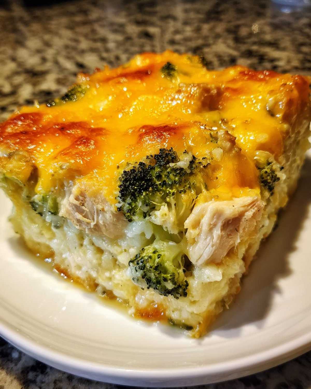 Close-up of a square slice of chicken broccoli rice casserole topped with melted, golden cheddar cheese.