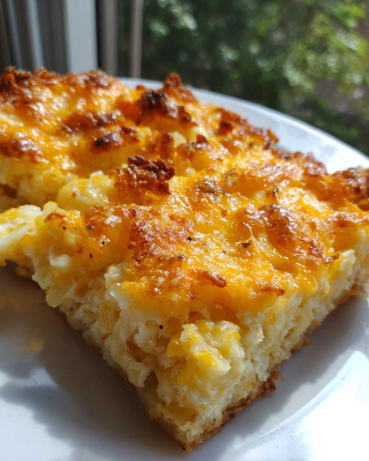 Close-up of a thick slice of cheesy potato casserole with a golden, bubbly, baked cheese crust.