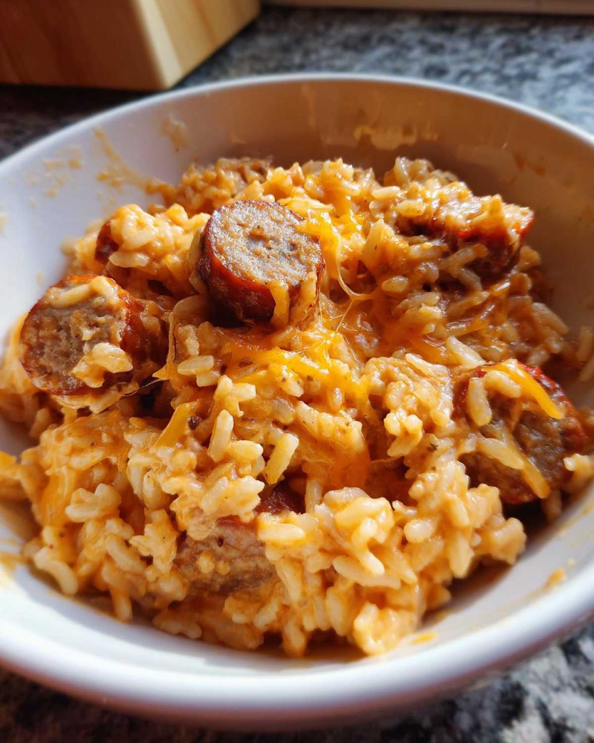 A close-up of a creamy, cheesy bowl of sausage and rice, featuring sliced, browned sausage pieces.