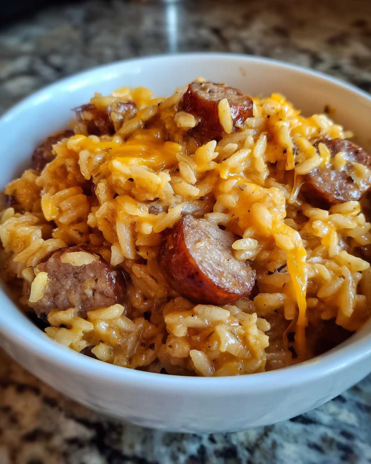 Close-up of creamy sausage and rice mixed with melted cheddar cheese served in a white bowl.