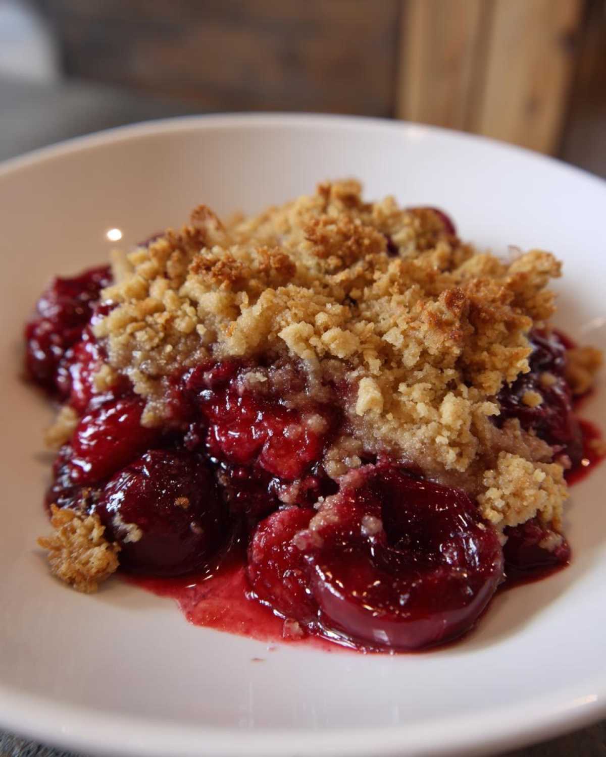 A close-up of a serving of cherry dump cake showing the bright red, juicy cherry filling beneath a crumbly, golden topping.