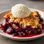 A close-up of a warm slice of cherry dump cake topped with a scoop of vanilla ice cream.