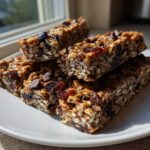 A stack of chewy no bake granola bars featuring oats, dried fruit, and visible chocolate chips, sitting on a white plate.