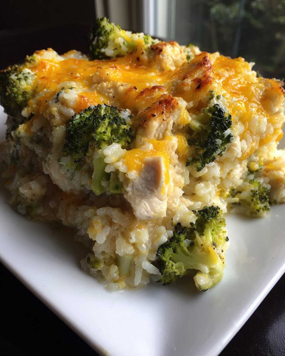 Close-up of a hearty serving of chicken broccoli rice casserole topped with melted, slightly browned cheddar cheese.