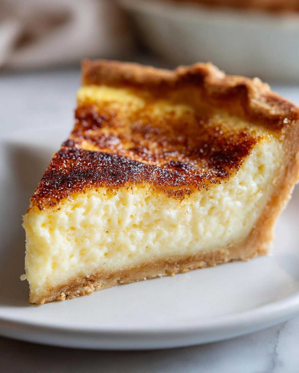 A close-up of a perfect slice of classic custard pie showing a creamy filling and a beautifully browned, sugary top.