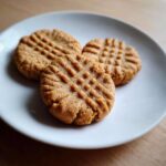 Close-up of three classic peanut butter cookies with fork crosshatch marks served on a white plate.