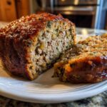 A moist, sliced loaf of classic stuffing with a shiny brown glaze resting on a white plate.