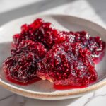 Close-up, vibrant image of thick, seedy raspberry jam glistening on a small plate.