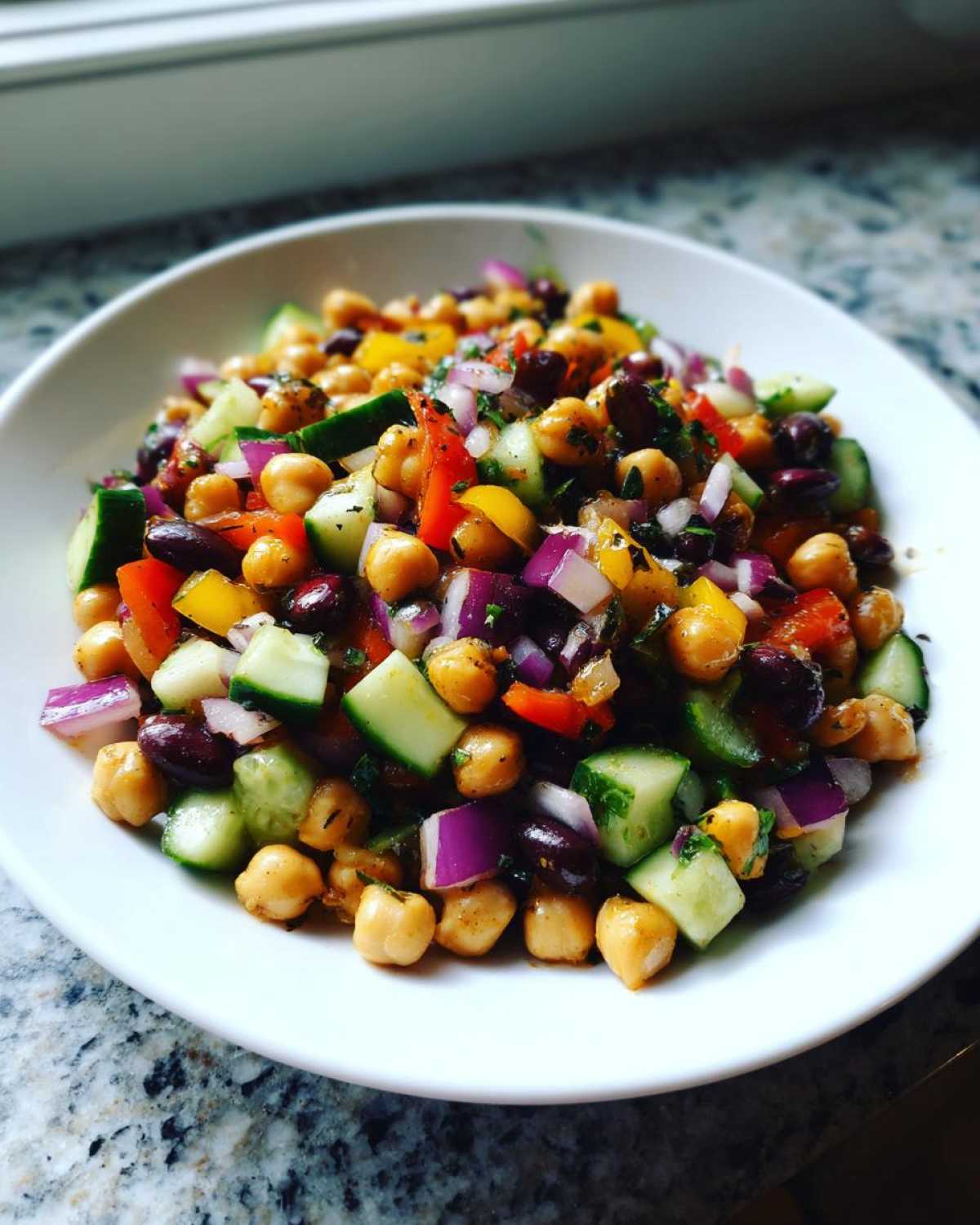 Close-up of a vibrant bean salad featuring chickpeas, red onion, cucumber, and bell peppers.