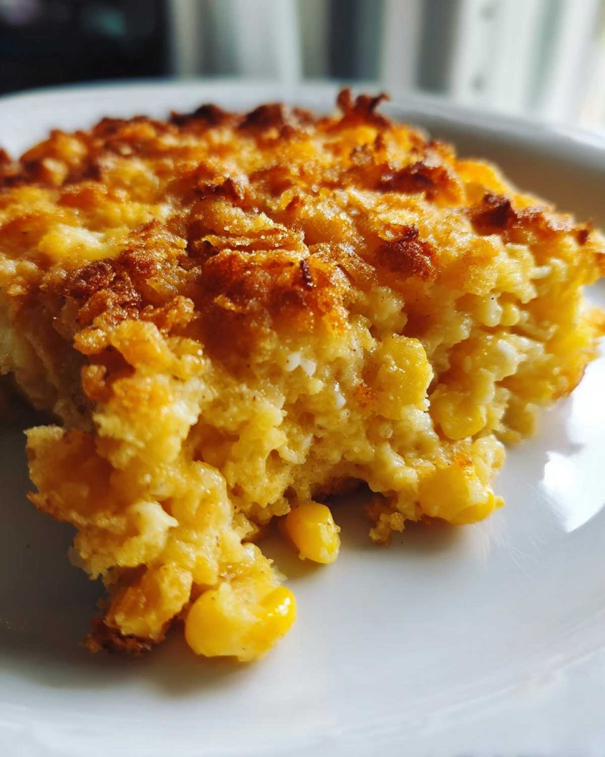 Close-up of a serving of creamy, golden cream cheese corn casserole with a crispy, browned topping.