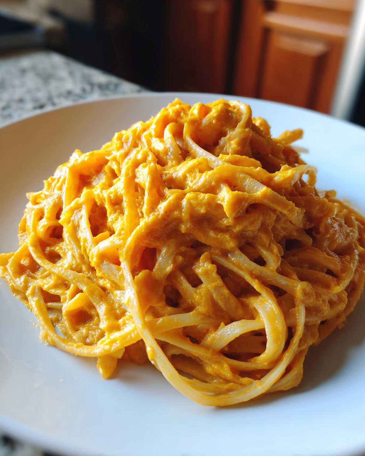 Close-up of spaghetti coated generously in a creamy orange butternut squash pasta sauce on a white plate.