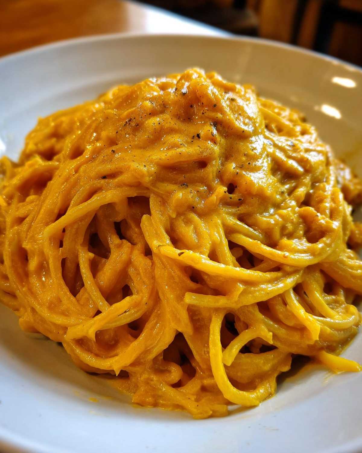 Close-up of spaghetti fully coated in a rich, creamy butternut squash pasta sauce, topped with black pepper.