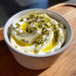 Close-up of creamy white dip topped with olive oil and chopped pistachios, ready to serve as dirty martini dip.