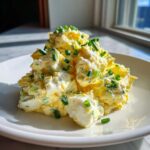A mound of creamy, chunky egg salad recipe topped generously with fresh chopped green chives on a white plate.