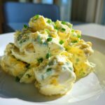 A mound of creamy, yellow egg salad recipe garnished with fresh green chives on a white plate.