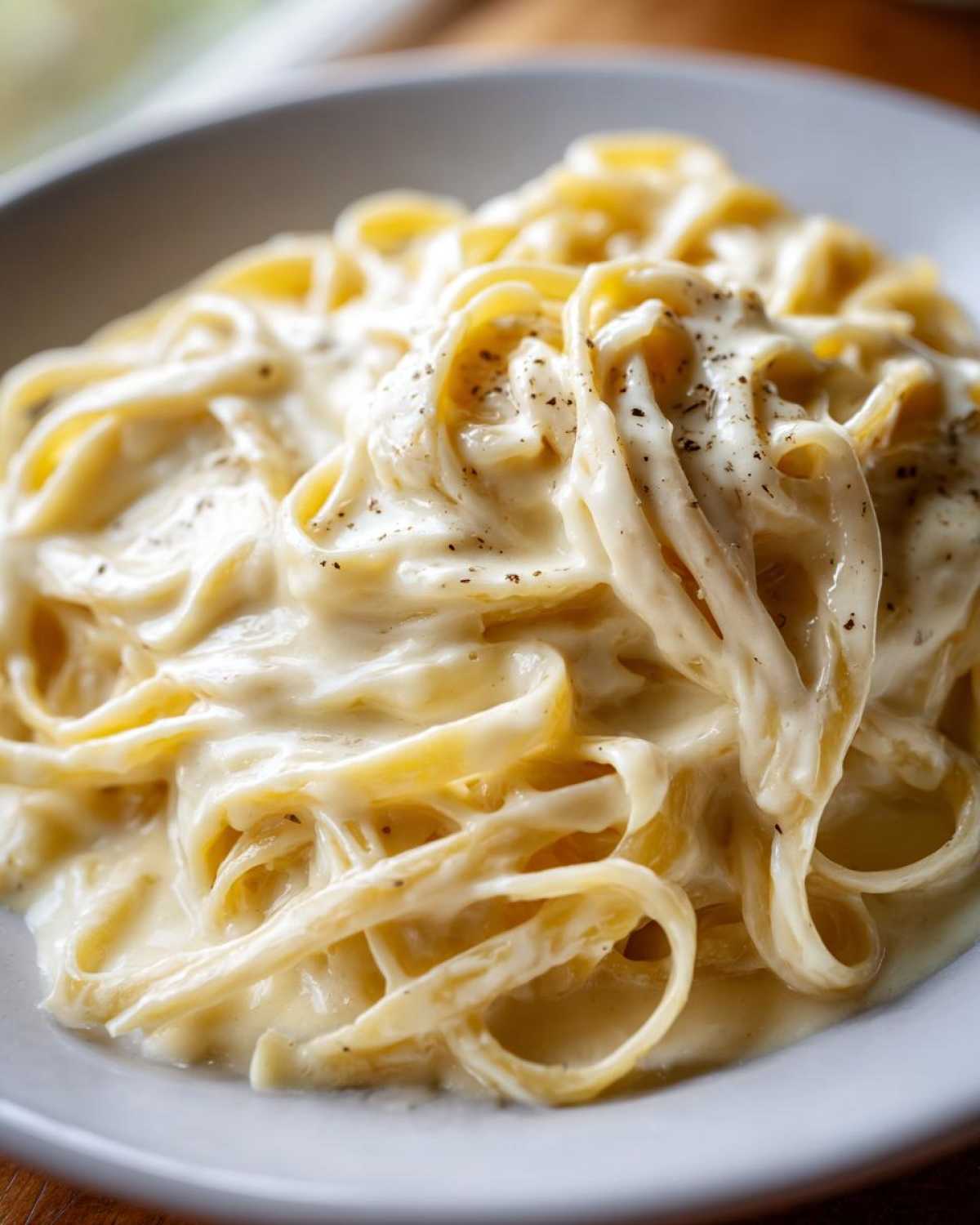 Close-up of fettuccine pasta generously coated in rich, creamy homemade alfredo sauce and sprinkled with black pepper.