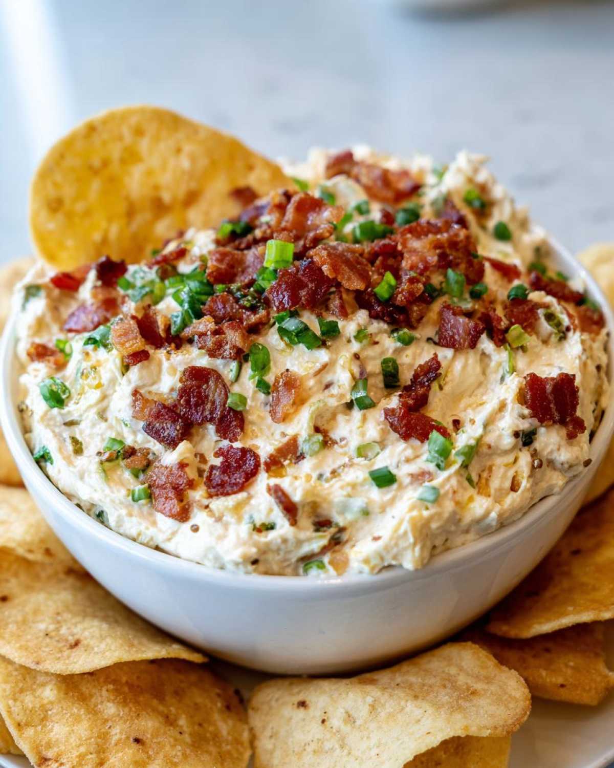 Close-up of a bowl of creamy Million Dollar Dip topped generously with crispy bacon bits and chopped green onions.