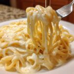 Close-up of fettuccine pasta coated in creamy olive garden alfredo sauce being lifted by a fork.