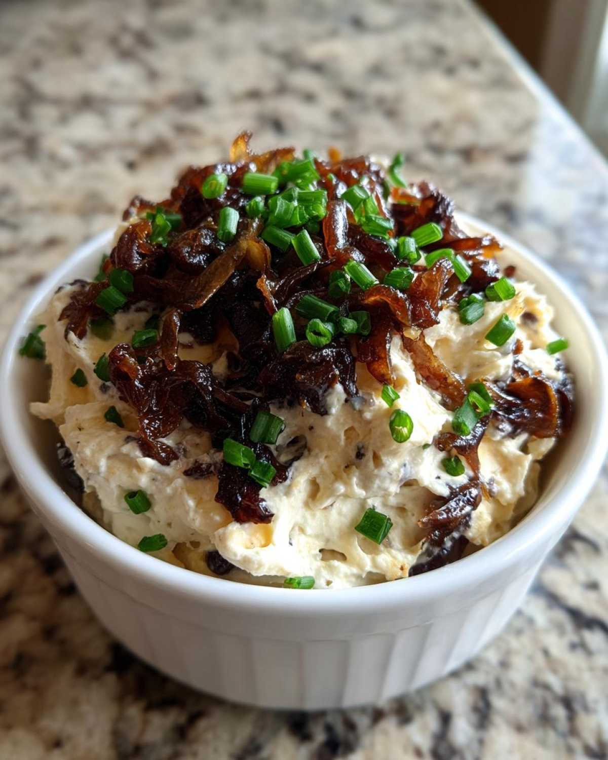 Close-up of creamy onion dip topped generously with dark caramelized onions and fresh green chives.