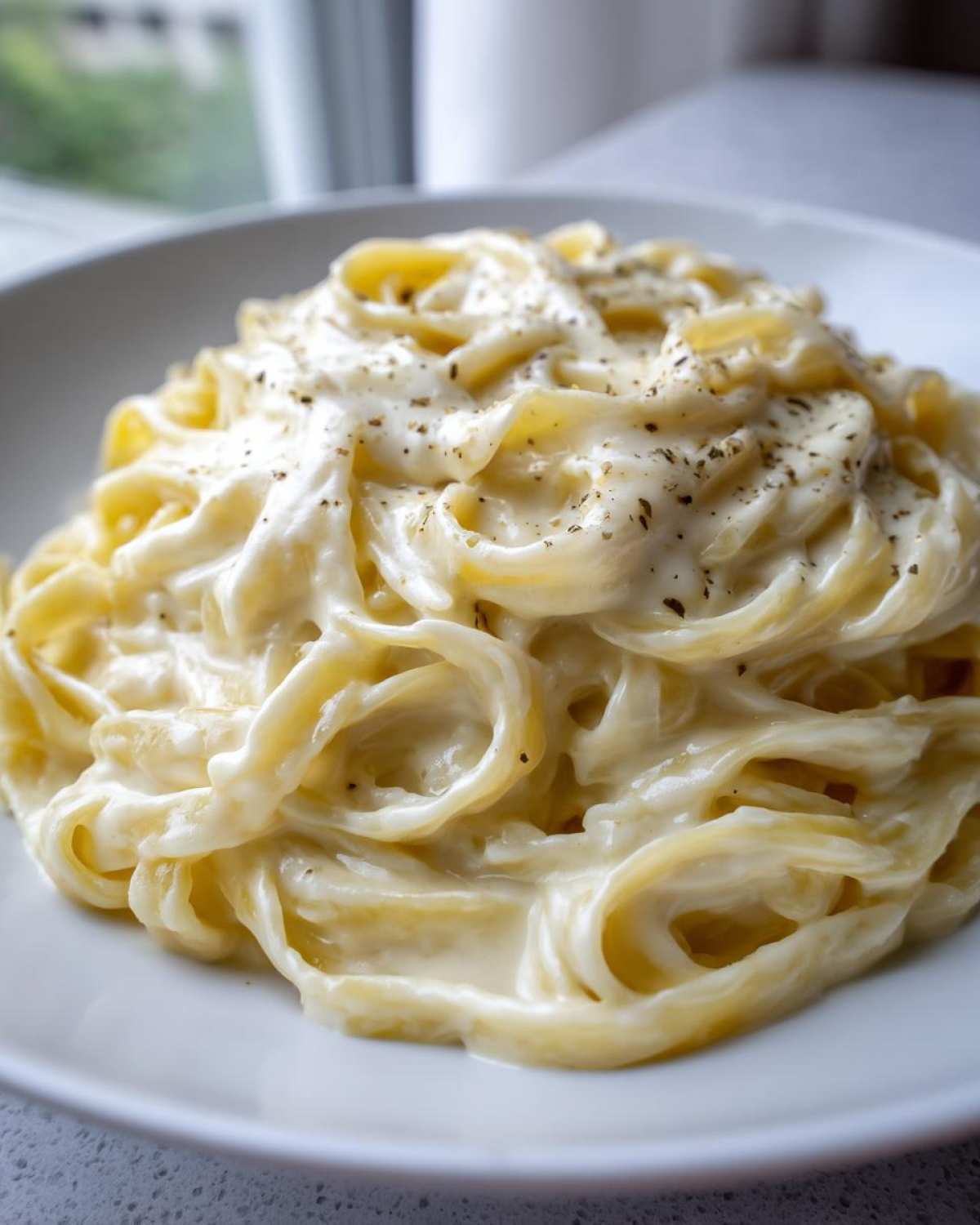 Close-up of fettuccine pasta generously coated in rich, creamy homemade alfredo sauce and sprinkled with pepper.