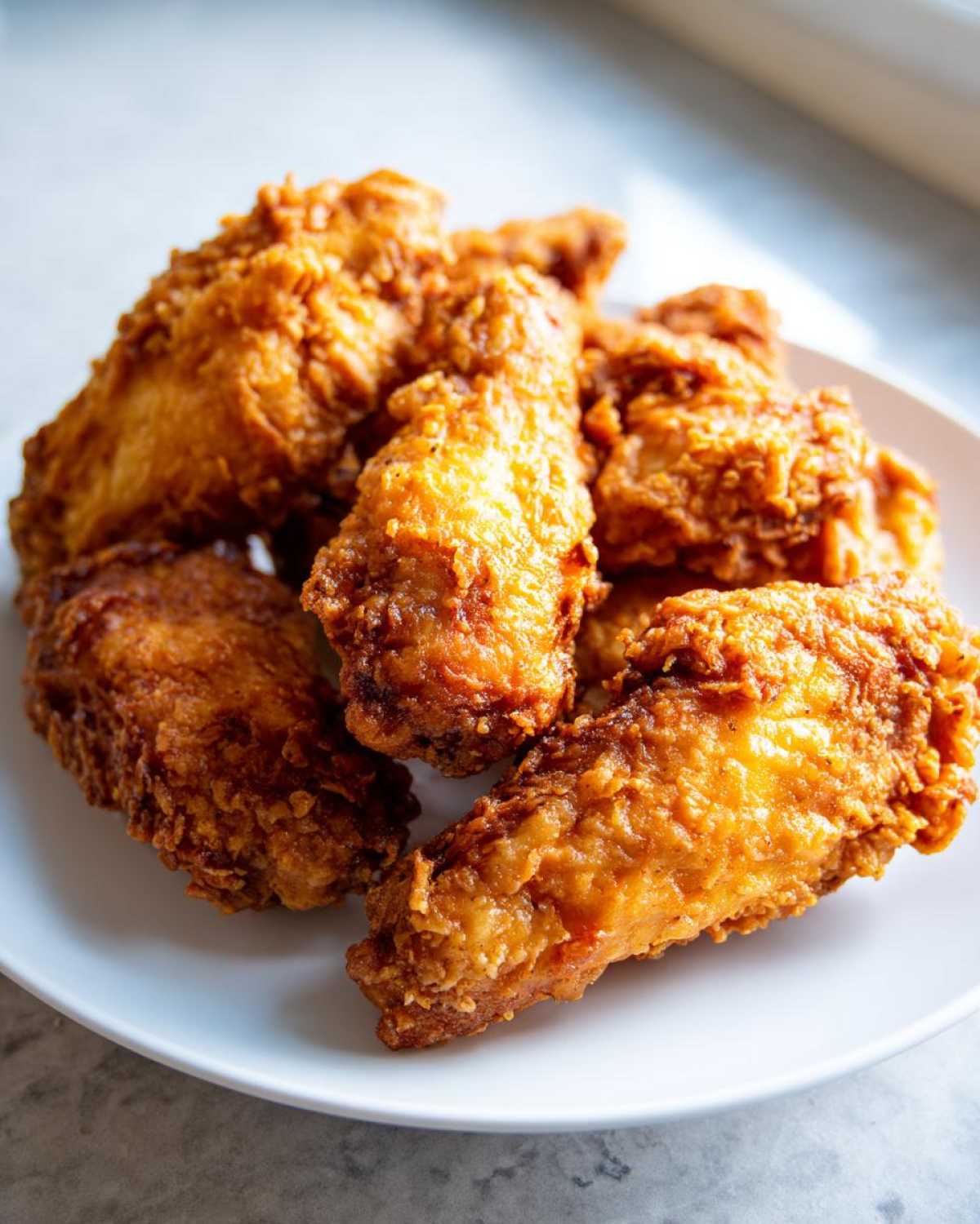 Close-up of several golden brown, crispy air fryer chicken wings piled on a white plate.