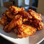 A pile of golden brown, glazed, crispy baked chicken wings served on a white plate.