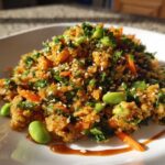 A mound of colorful crispy rice salad mixed with bright green edamame, carrots, herbs, and sesame seeds.