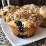 A close-up of a golden baked blueberry muffin topped with generous cinnamon streusel crumbs.