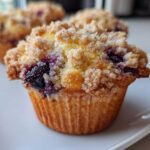 Close-up of a golden-brown blueberry muffin featuring a generous, sugary crumb topping and visible baked blueberries.