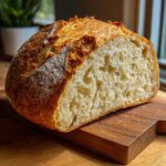 A close-up of a freshly baked Italian bread loaf, cut in half to show the open, airy crumb structure.