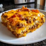 A close-up of a square serving of Dorito Casserole layered with ground meat and topped with melted, bubbly cheddar cheese.