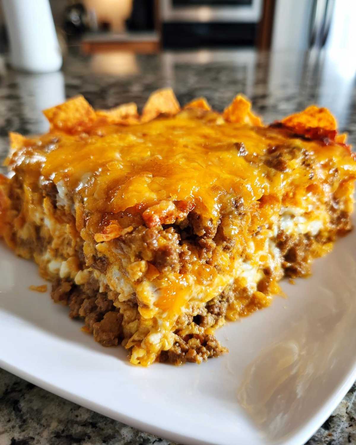 Close-up of a hearty slice of Dorito Casserole layered with ground beef, creamy sauce, and topped with melted cheddar cheese and chips.