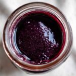 Overhead view of thick, dark purple elderberry syrup recipe inside a clear glass jar.