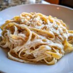 Close-up of fettuccine pasta generously coated in rich homemade alfredo sauce and sprinkled with black pepper.