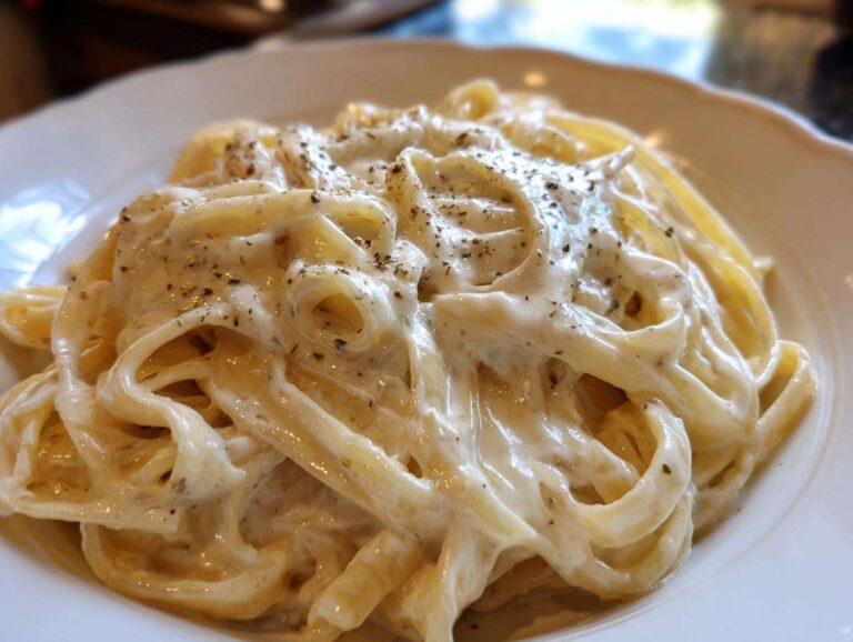Close-up of fettuccine pasta generously coated in creamy homemade alfredo sauce and topped with cracked black pepper.