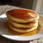 A stack of three fluffy almond flour pancakes drizzled with syrup on a white plate.