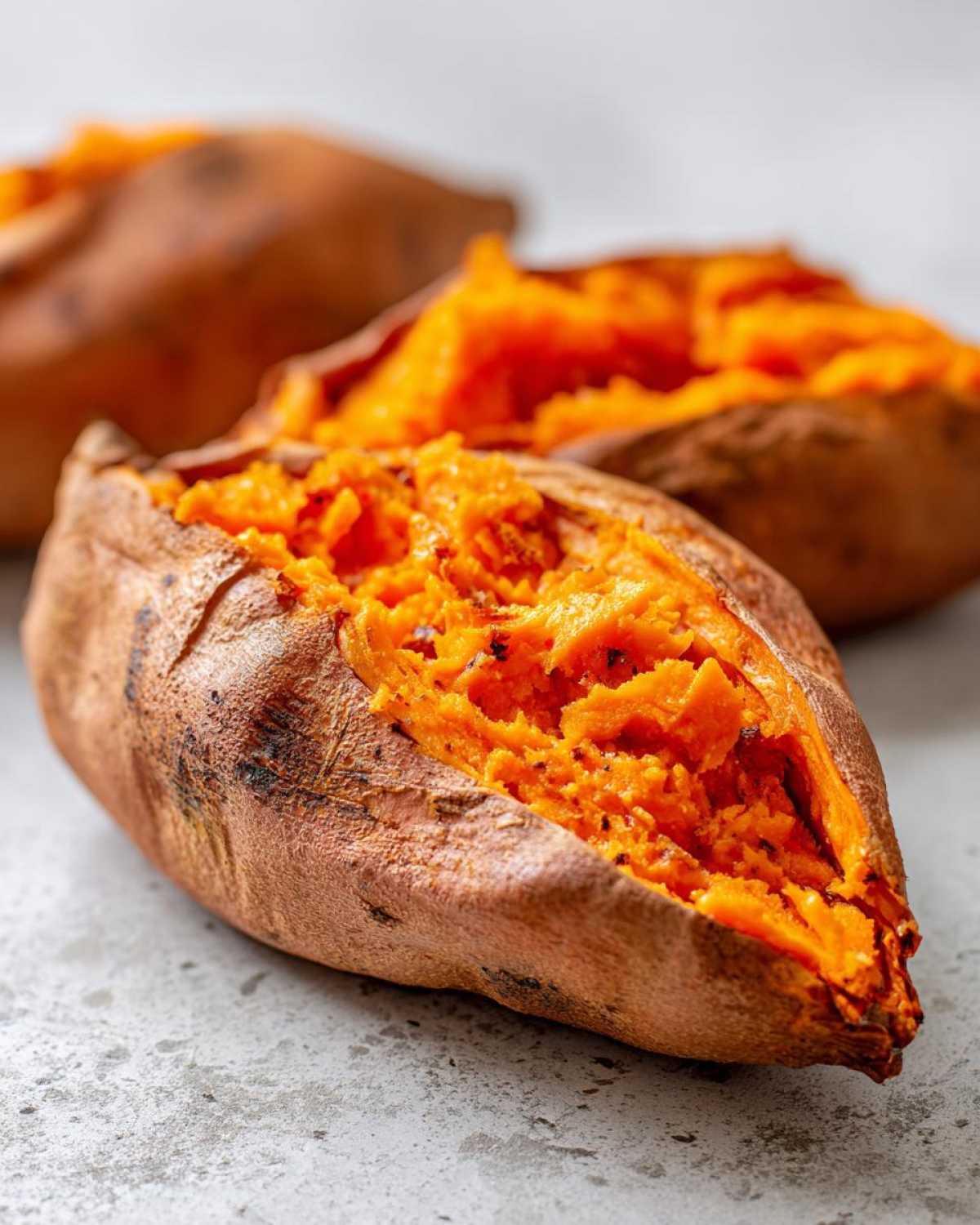 Close-up of a fluffy baked sweet potato split open, revealing bright orange, mashed interior.