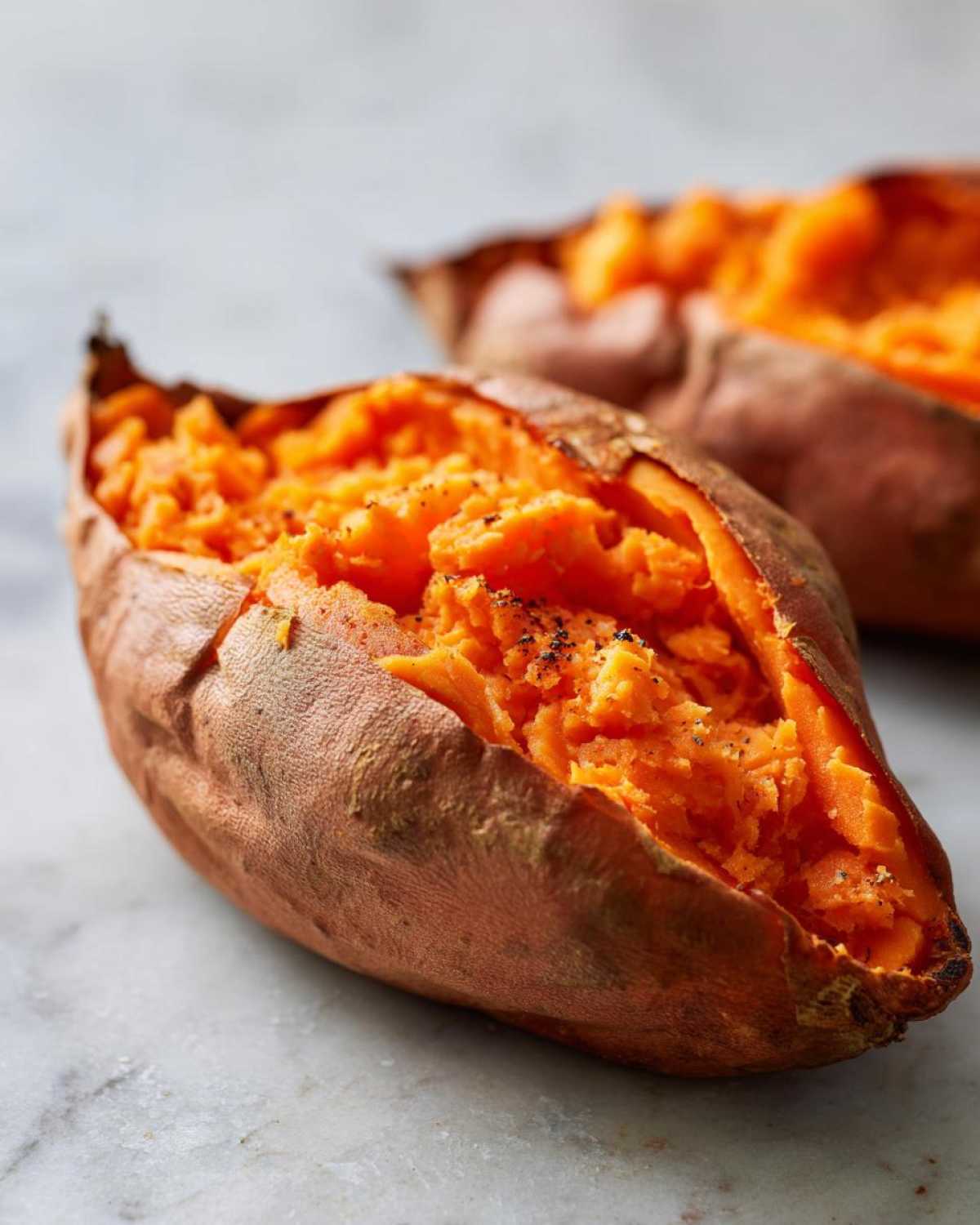 Close-up of fluffy baked sweet potatoes, split open and seasoned with cracked black pepper.