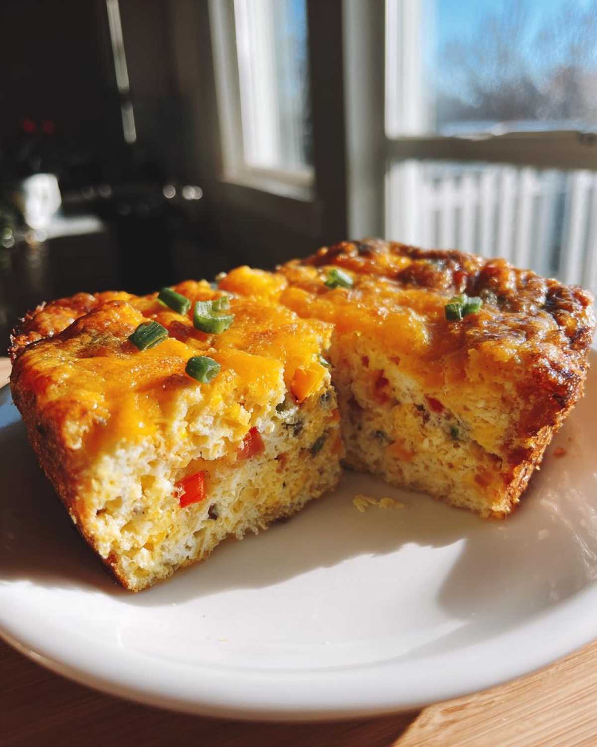 A fluffy portion of 12-egg bake, cut in half, showing colorful vegetables and melted cheddar cheese topping.