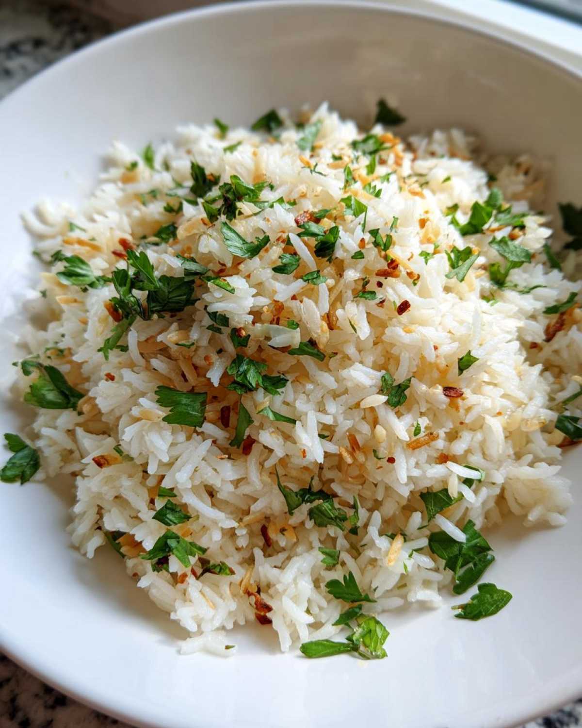 A close-up of fluffy white rice pilaf garnished generously with fresh chopped parsley and toasted bits.