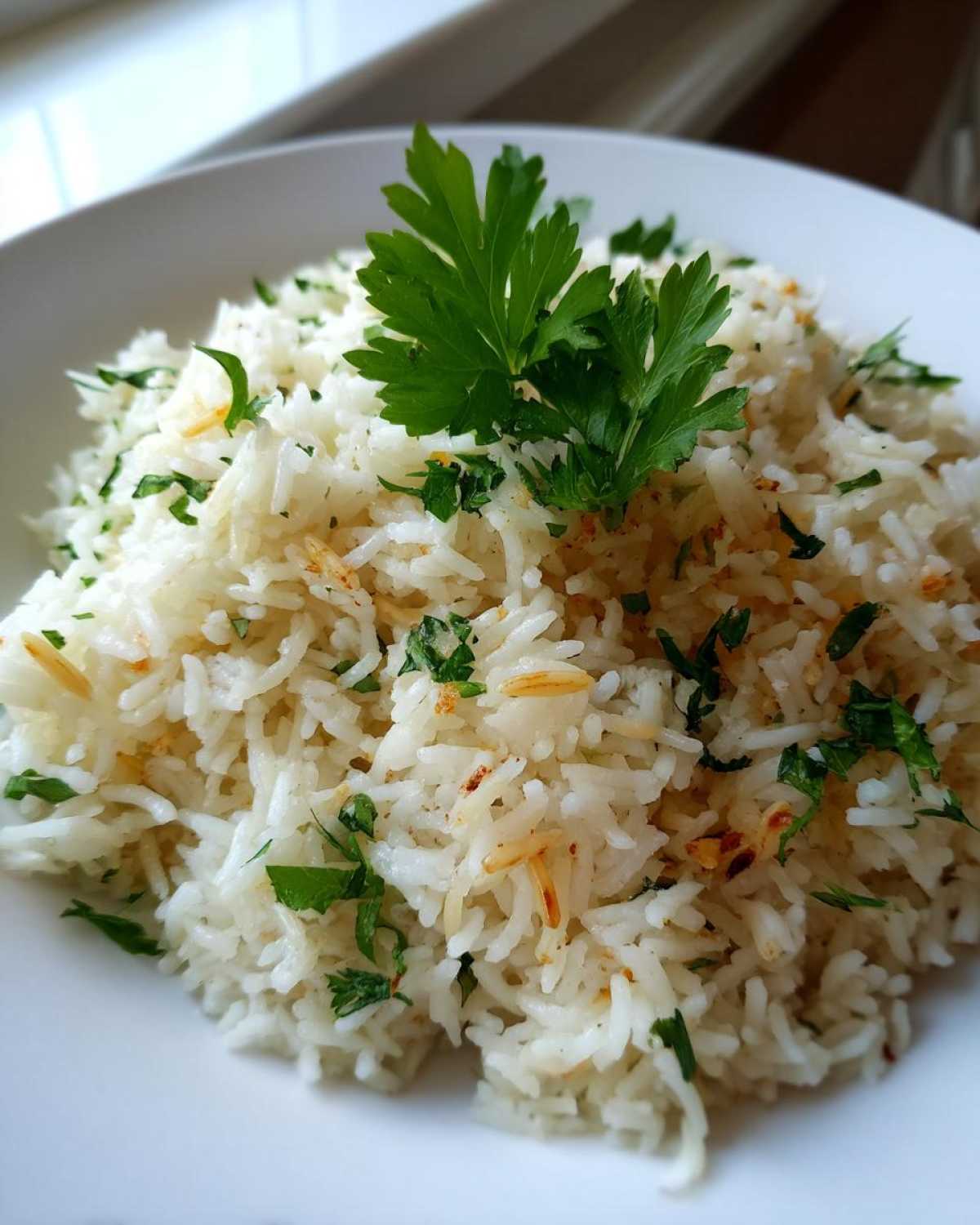 Close-up of fluffy white rice pilaf garnished with chopped parsley and a sprig of fresh parsley on top.