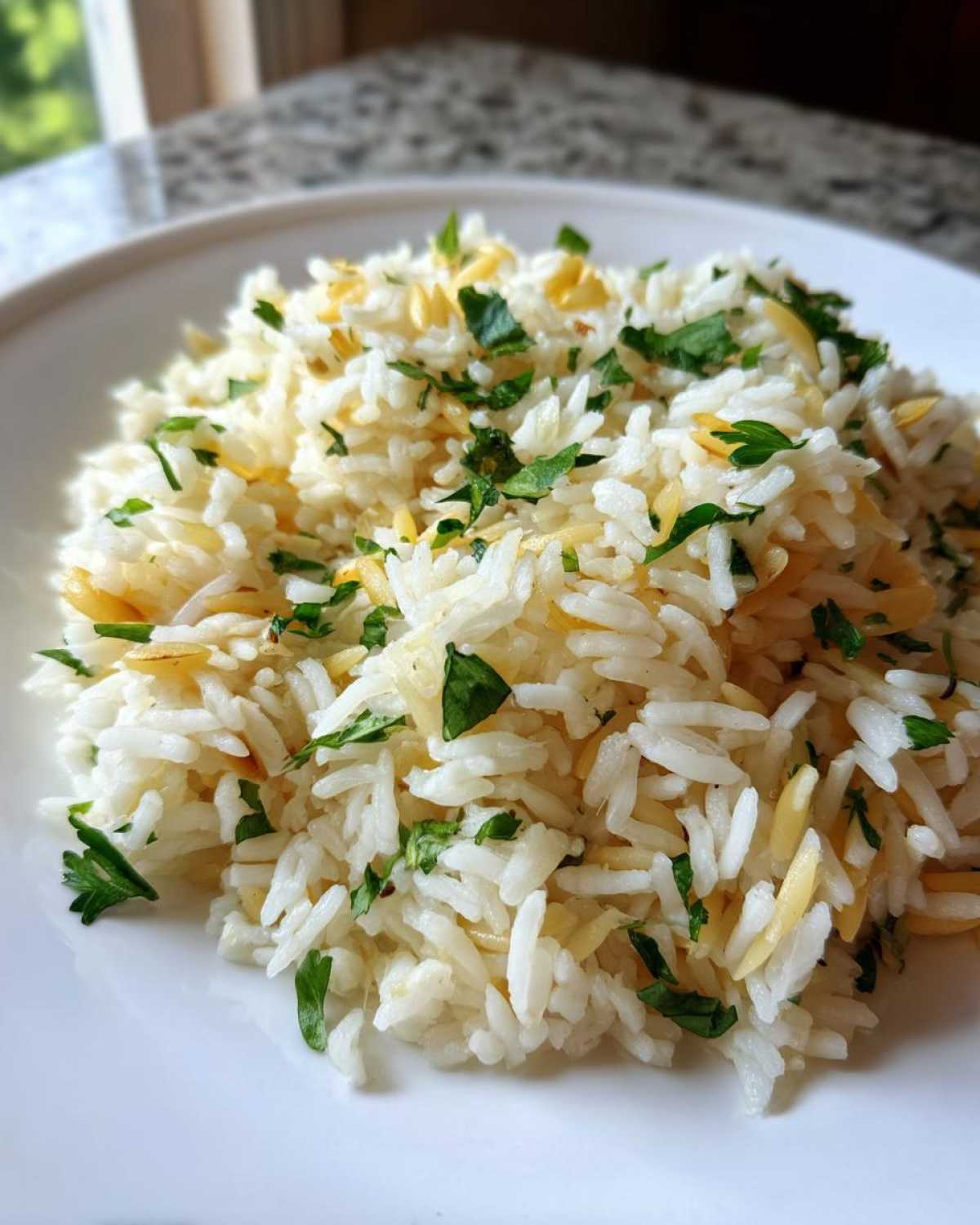 Close-up of fluffy rice pilaf mixed with toasted orzo pasta and topped with fresh chopped parsley.